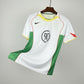 White sports jersey with green and red accents on a hanger against a black mesh background