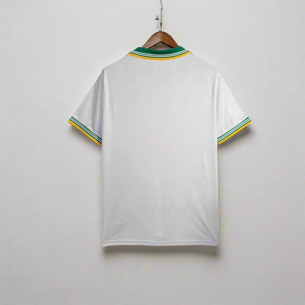 White sports jersey with green and yellow accents hanging on a rack.